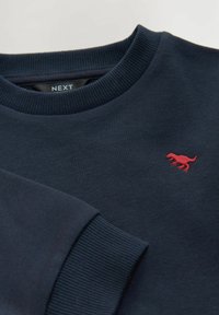 Sweatshirt bleu marine, en mélange de coton, avec un col et des poignets côtelés, et un petit logo de dinosaure rouge brodé sur la poitrine.