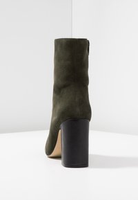 Olivově zelené semišové kotníkové boty s elegantním tvarem, černým masivním podpatkem a hladkým vnitřním podšíváním. Obsahují boční zip.