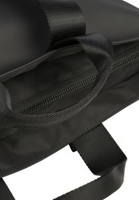 Zwarte tas met een gladde, matte afwerking en een leren band. Bevat een ritsvak en robuuste stiksels op de naden.
