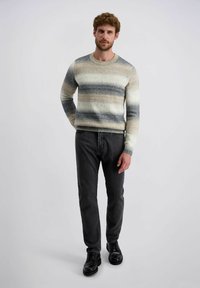 Gebreide trui met horizontale strepen in beige, grijs en blauwtinten, met een geribbelde ronde hals. Gecombineerd met donkere jeans en zwarte schoenen.