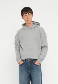 Grå hættetrøje lavet af blødt stof, med en frontlomme og manchetter, parret med blå denimjeans.