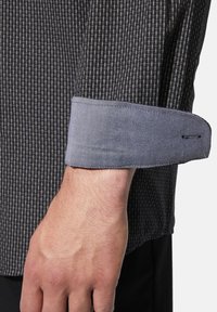 Grau gemustertes Hemd mit einem dunklen Karodesign und einem kontrastierenden hellgrauen Manschette. Die Manschette ist glatt mit einem dezenten Stichdetail.