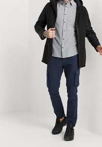 Zwarte hoodie-jack over een grijs en zwart geblokt shirt, gecombineerd met marineblauwe cargobroeken en zwarte sneakers. Casual stijl met functionele zakken.