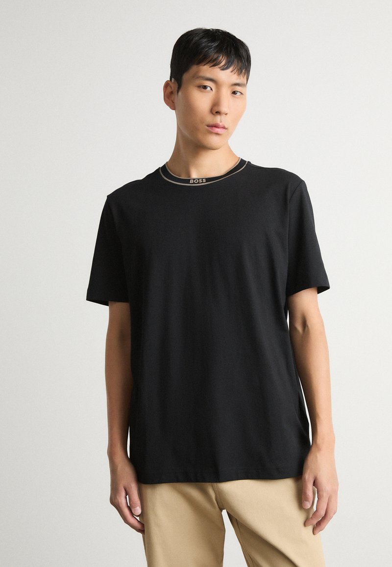 Juodas trumpas rankovėmis T marškinėliai, pagaminti iš medvilnės, su apvalia iškirpte, išsiskiriantys kontrastingu siuvinėtu logotipu ant apykaklės. Paprastas dizainas, laisvas kirpimas.