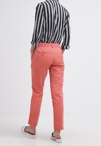 Różowe spodnie z lekkiego materiału o slim fit, zestawione z czarno-białą wąską koszulą. Widoczne tylne kieszenie i swobodne obuwie.