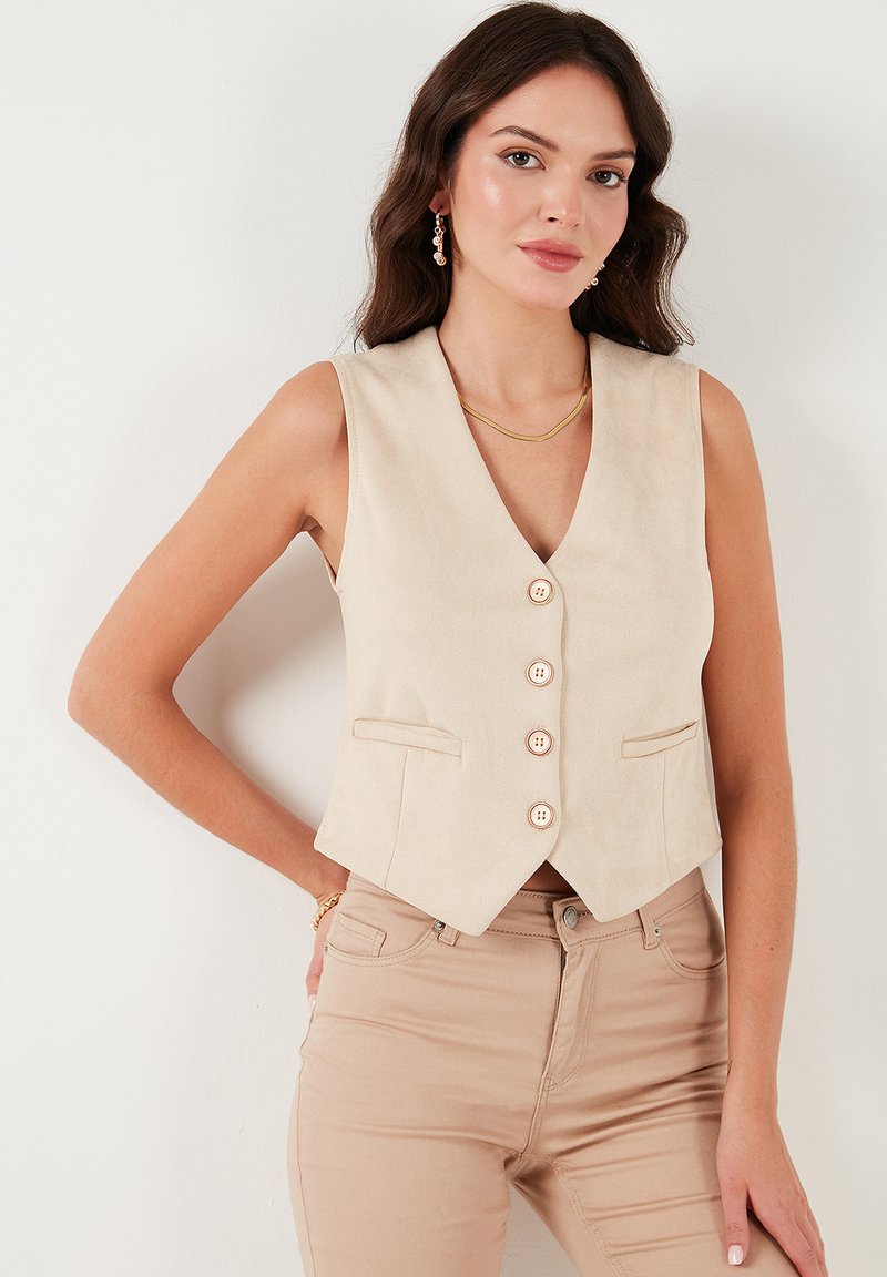 Chaleco sin mangas beige con escote en V, cinco botones y dos bolsillos delanteros, hecho de una tela suave, combinado con pantalones ajustados beige claros.