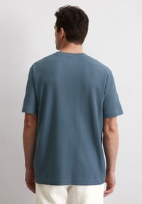 Blauw T-shirt met korte mouwen van een textuurstof, crewneck en rechte zoom. De achterkant toont minimale details en een relaxte pasvorm.