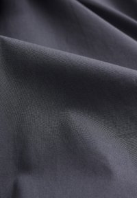 Temno sivo blago z gladko teksturo, ki prikazuje subtilen sijaj in gube, kar ustvarja mehak učinek drape. Brez vidnih vzorcev ali dodatkov.