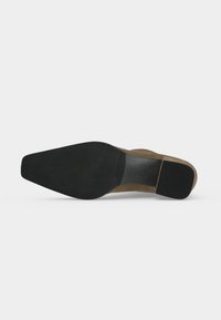 Semelle d'une chaussure de ville en daim marron avec un bout pointu noir lisse et un talon noir rectangulaire sur fond blanc.