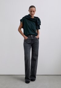 Dark green short-sleeve t-shirt with a relaxed fit, paired with high-waisted, dark gray wide-leg jeans. Accented with a dark sweater draped over the shoulders.