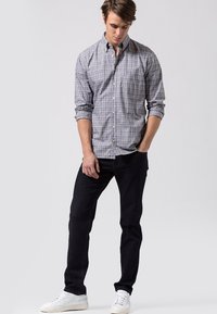 Camisa de cuadros en azul, blanco y gris; combinada con jeans oscuros y zapatillas blancas. Presenta mangas enrolladas y un único bolsillo en el pecho.