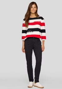 Langärmliges Oberteil mit rot, weiß und schwarz gestreiftem Design und dem Wort "INSPIRE" in Rot; kombiniert mit schwarzen Hosen und weißen Sneakern.