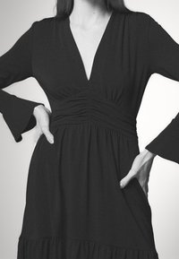 Abito nero con scollatura a V profonda, maniche a campana lunghe e corpetto arricciato, caratterizzato da una gonna ampia e una texture sottile.