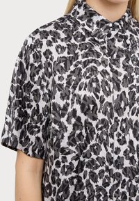 Camicia a maniche corte in tessuto leggero con motivo stampa animale in bianco e nero. Collo classico con dettaglio dei bottoni.