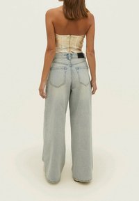 Lichte blauwe jeans met wijde pijpen en een vervaagde textuur, voorzien van een hoge taille, twee achterzakken en een subtiele logo-label nabij de tailleband.