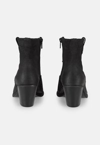 Botas de tobillo negras con acabado de ante, que cuentan con un tacón bloque de altura media y cremalleras laterales. Tienen una textura suave y detalles de costura sutil.