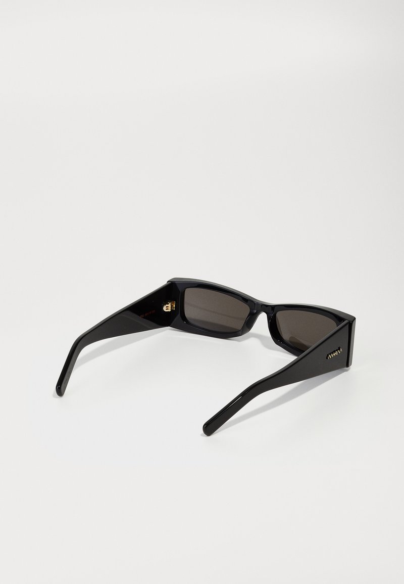 Lunettes de soleil noires avec des verres rectangulaires, monture épaisse en plastique et temples fins. Présente un petit accent doré sur le côté.