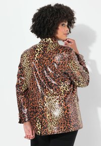 Leopardmönstrad blazer i glansigt tyg med orange, bruna och gula nyanser, raglankrage och två knappar på ärmarna.