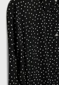 Chemise noire à manches longues avec un motif irrégulier de petits pois blancs.