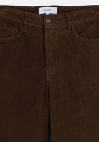 Pantalones de pana marrones con una superficie texturizada, bolsillos frontales, cierre de botón y una etiqueta con "SCALPERS" en la cintura.