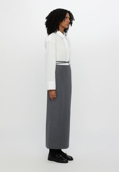 Camisa blanca de manga larga, ajustada con botones; falda larga gris de material suave con corte recto; zapatos negros con hebillas.