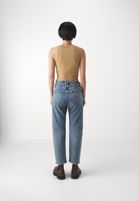 Brązowa prążkowana bluzka bez rękawów w połączeniu z jasnoniebieskimi dżinsami z wysokim stanem. Całość dopełniają ciemnobrązowe botki za kostkę.