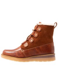 Botín de cuero marrón con acentos de ante, forrado de piel sintética, puntera redonda y diseño de cordones. Incluye una suela de goma gruesa y herrajes en tono dorado.