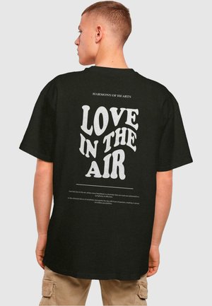 Black cotton t-shirt featuring large white text on the back with the phrase "LOVE IN THE AIR" and smaller text above and below it.