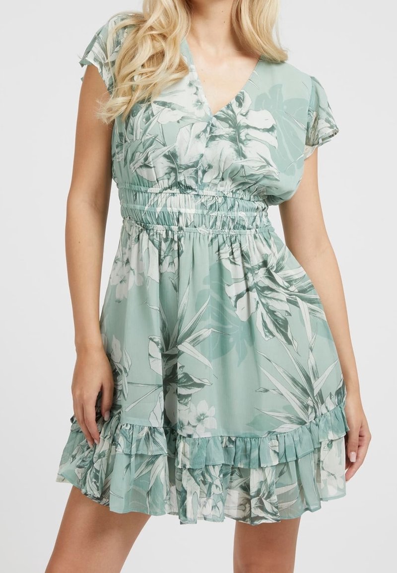 Robe florale en tissu vert clair, avec un col en V, des manches courtes, une taille élastique et un ourlet à volants superposés, ornée de motifs de feuilles tropicales et de fleurs.