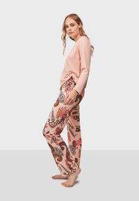 Rosa Langarmoberteil kombiniert mit gemusterten Hosen, die florale und Paisleymuster in rosa, rot und braun zeigen. Weicher Stoff.