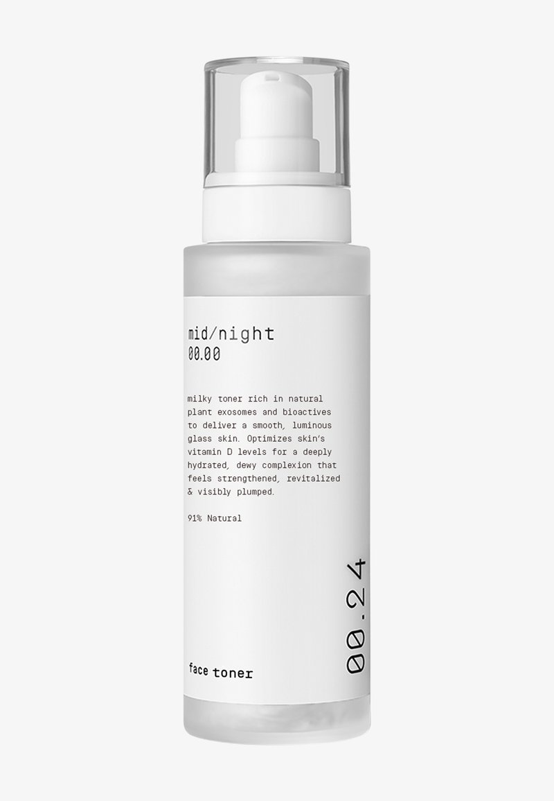 Klar glassflaske med en hvit pumpehett, merket med svart tekst. Flaska inneholder en melkeaktig toner med et elegant, minimalistisk design.