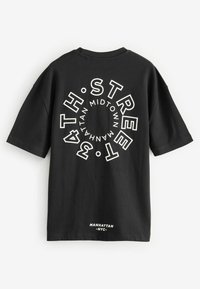 Sort bomulds t-shirt med stort hvidt cirkulært grafik tekst på ryggen. Teksten inkluderer "34TH STREET," "MIDTOWN," og "MANHATTAN."