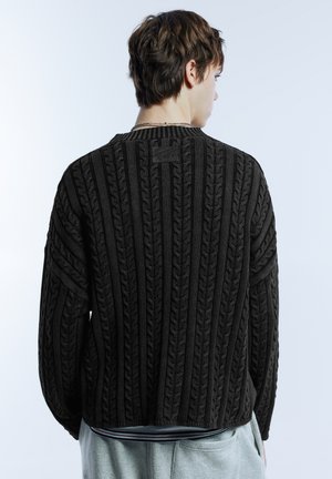 Dunkler gestrickter Pullover mit Zopfmuster, geripptem Kragen und Bündchen. Verfügt über ein kleines Logotag auf der Rückseite. Lockerer Schnitt.