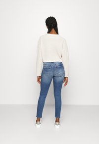 Lys beige cropped sweater med tekstureret stof, parret med slim-fit blå jeans. Hvide sneakers har grå accenter og et logo.