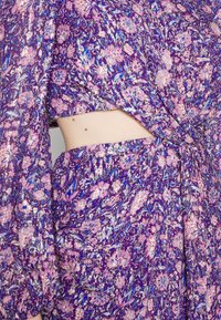 Fialové květinové šaty s růžovými a modrými vzory, lehká látka s lesklým povrchem, krátký střih a zauzlený detail v pase.