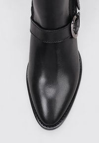 Bottine en cuir noir avec un embout pointu, une finition lisse et un détail de boucle sur le côté. Présente une semelle cousue pour plus de durabilité.