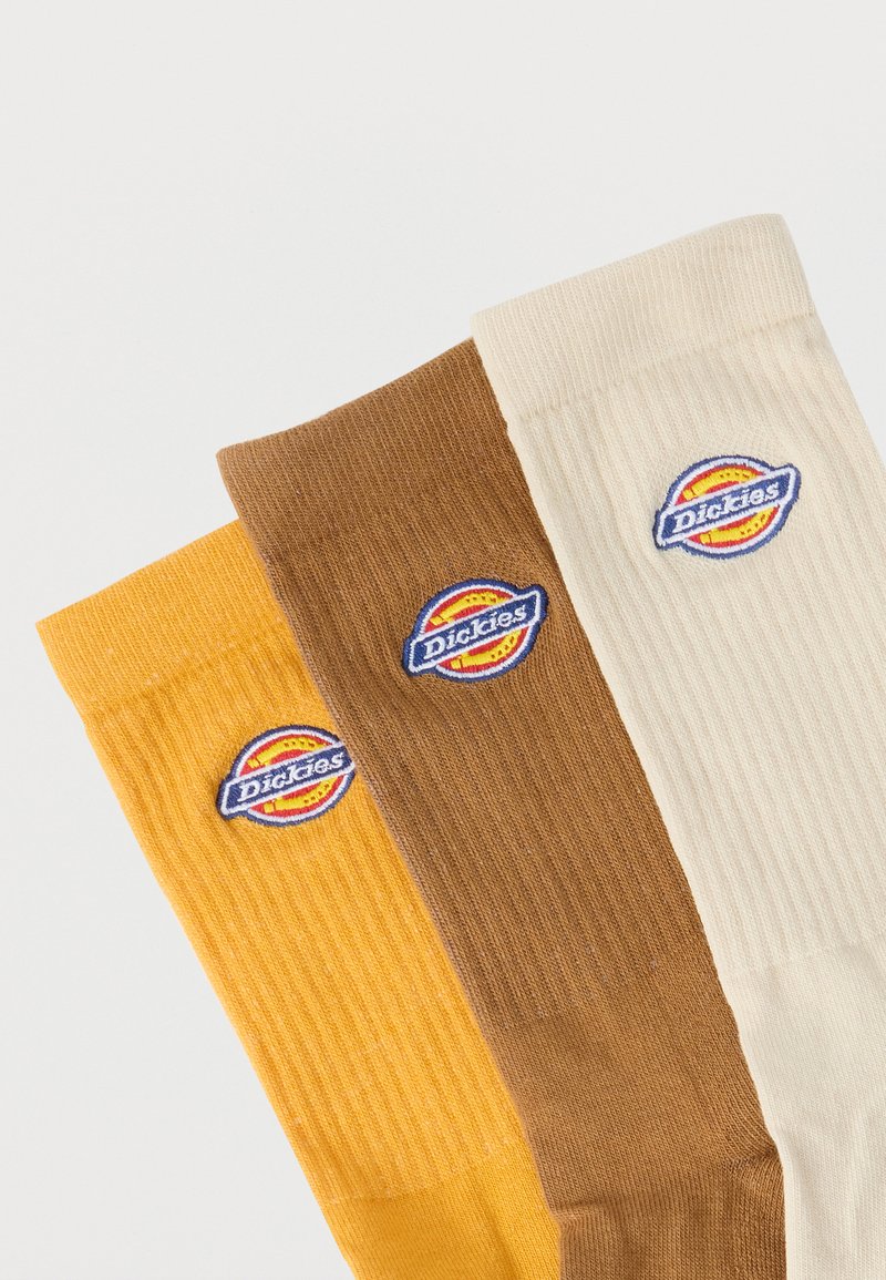 Three folded ribbed socks in yellow, brown, and cream, each featuring a circular Dickies logo patch near the cuff.