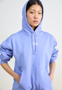 Felpa con cappuccio di colore lilla chiaro, dotata di tasca frontale, con un logo bianco sul petto e polsini elasticizzati. Tessuto morbido e vestibilità rilassata.