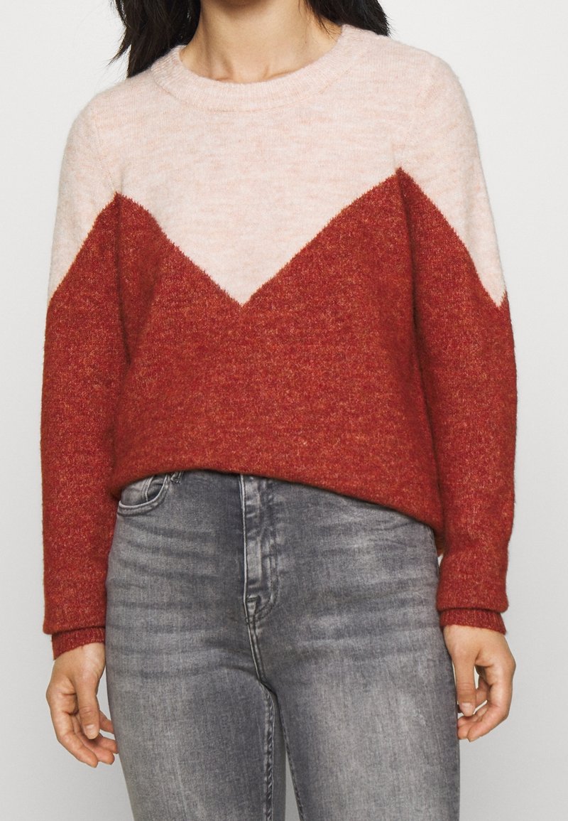 Röd och rosa färgblockerad tröja med ett chevronmönster, tillverkad av ull, med rundhals och ribbade ärmar.