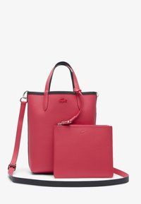 Sac tote en cuir rouge avec une finition texturée, présentant des accents noirs et une pochette amovible. Comprend des poignées courtes et une bandoulière.
