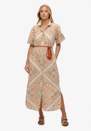 Mujer que lleva un vestido midi con estampado floral, mangas cortas, cuello alto, cierre de botones en la parte delantera y un cinturón trenzado de color óxido con borlas.