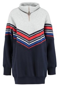Suéter de pulóver en gris claro y azul marino con cuello de cremallera, que presenta un patrón de chevron en franjas rojas, blancas y azules a lo largo del pecho.