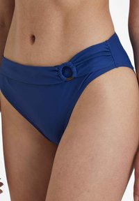 Bas de bikini bleu marine avec taille large, tissu froncé et accent circulaire doré sur le côté. Texture lisse, design taille haute.