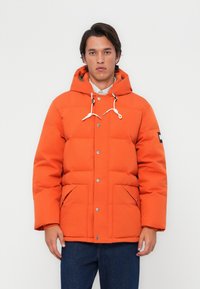 Bright orange puffer jacket with a hood, featuring white drawstring accents, side pockets, and a button-up front. Textured quilted design.