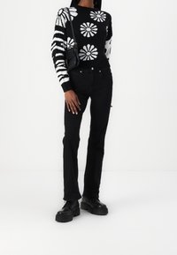 Woman wearing black and white floral and striped sweater, black jeans, black platform boots, and carrying a black shoulder bag.