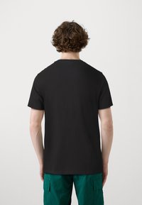 T-shirt noir à manches courtes dans une coupe classique, fabriqué en tissu lisse. Porté avec un short cargo vert avec des poches latérales.