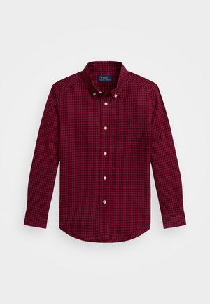 Raudona languota ilgaa rankovė švarko marška su mygtukų apykakle, baltais mygtukais ir mažuoju siuvinėtų logotipu kairėje krūtinės pusėje. Pagaminta iš medvilnės.