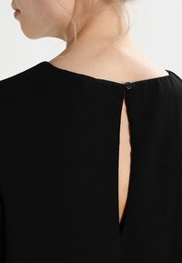 Robe noire avec un dos à trou de serrure et une fermeture à bouton. Le tissu est lisse, avec un design épuré et minimaliste, et un décolleté régulier.
