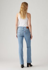 Light blue denim flared jeans feature a high waist, classic five-pocket design, and a brown leather label at the back. Smooth texture.