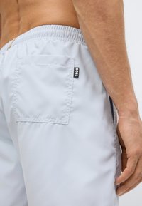 Ανοιχτό γκρι μαγιό σορτς με ελαστική μέση, πλαϊνή τσέπη και πίσω τσέπη με μια μικρή μαύρη ετικέτα "BOSS". Λείο υφασμάτινο ύφασμα.